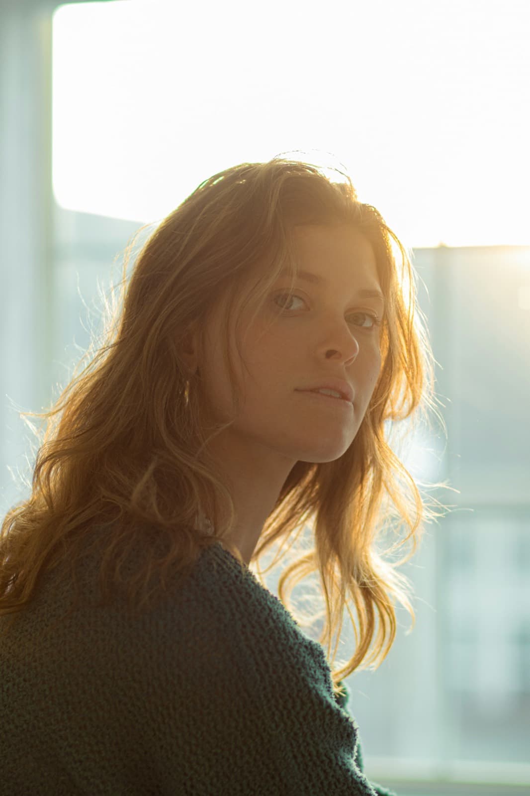 A woman in warm golden window light, lost in thought